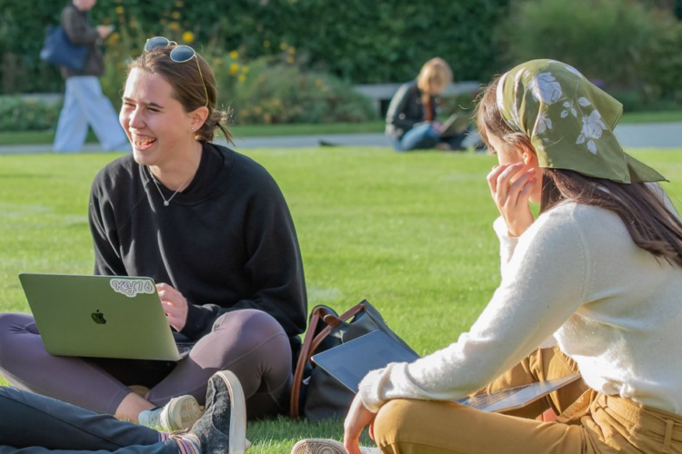 Two learners sitting on grass with a laptop